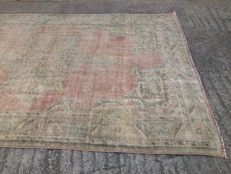 May include: A vintage rug with a faded pink and green floral pattern. The rug has a distressed look and is made of a soft, woven material.