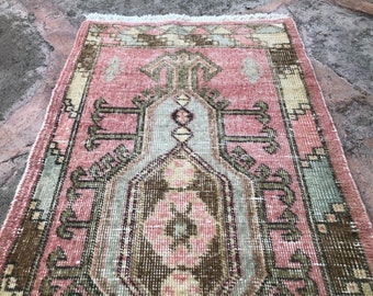 May include: A vintage pink and green rug with a geometric pattern. The rug has a fringe border and is made of wool.