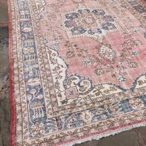 May include: A vintage pink and blue rug with a floral pattern and intricate border. The rug has a faded, distressed look and is made of a soft, woven material.