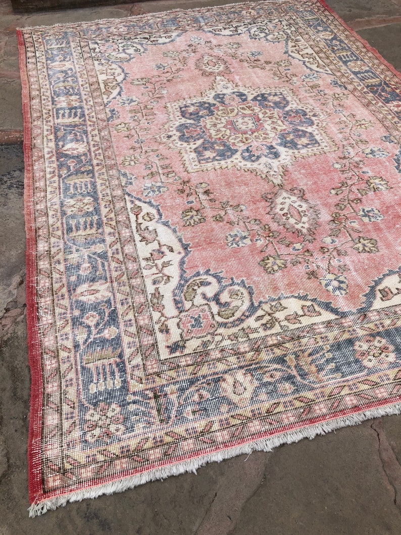 May include: A vintage pink and blue rug with a floral pattern and intricate border. The rug has a faded, distressed look and is made of a soft, woven material.