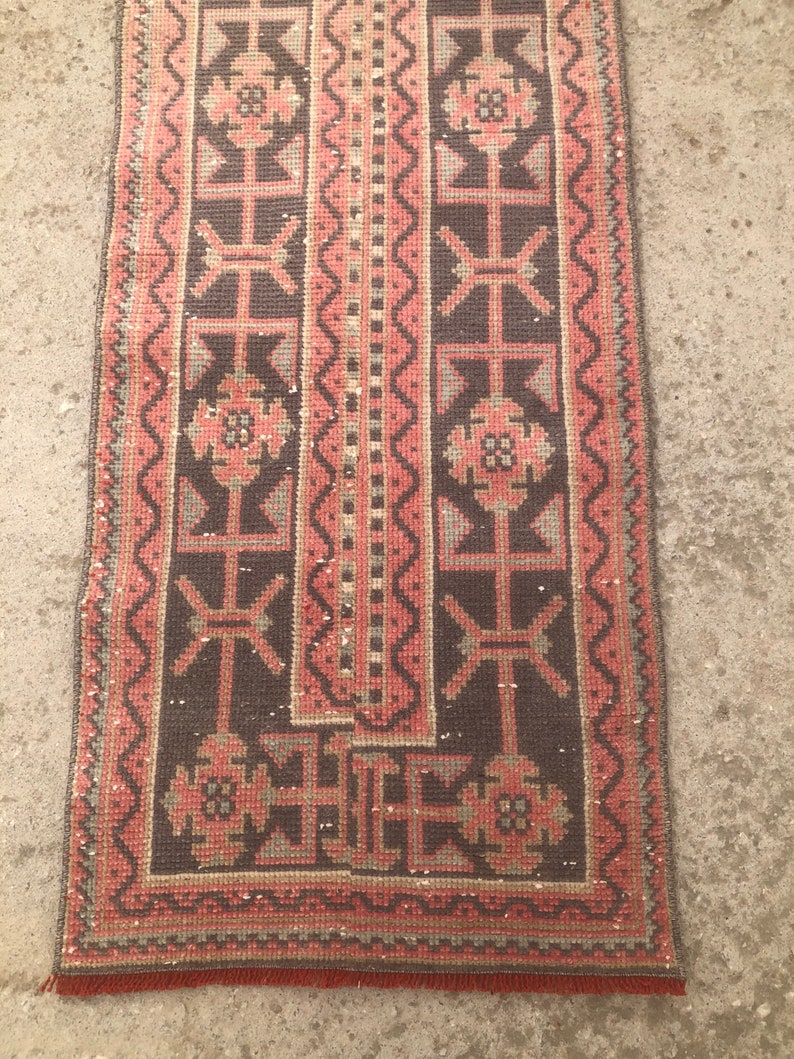 May include: A long, narrow rug with a dark brown background and a pink and gray geometric pattern. The rug has a fringe border. color on images may slight be different from the real rug