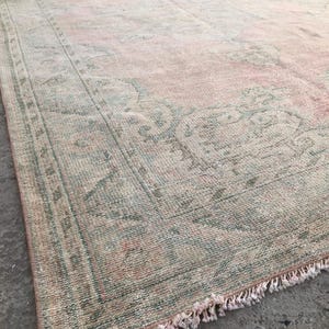 May include: A vintage rug with a faded pink and green floral pattern. The rug has a fringed edge and is made of a soft, woven material.