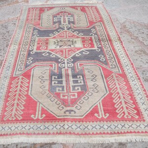 May include: A vintage Turkish rug with a red, beige, and black geometric pattern. The rug has a fringe border and is in good condition.