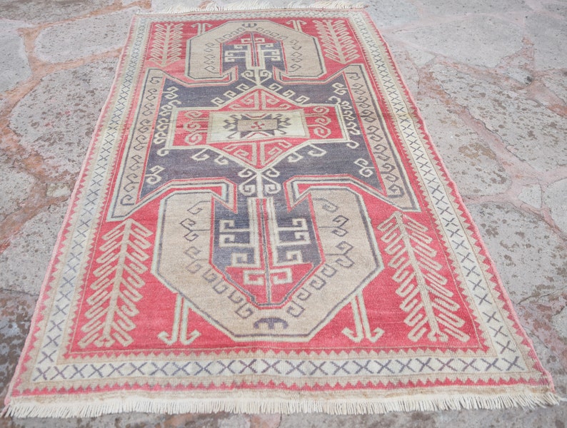 May include: A vintage Turkish rug with a red, beige, and black geometric pattern. The rug has a fringe border and is in good condition.