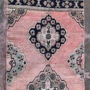 May include: A pink and black patterned rug with a traditional design. The rug has a fringe border and features intricate floral motifs.