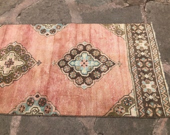 May include: A pink and brown vintage rug with a floral pattern. The rug has a faded look and a fringed edge.