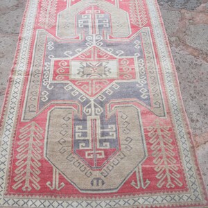 May include: A vintage Turkish rug with a geometric pattern in shades of red, beige, and gray. The rug has a fringe border and is woven with intricate details.