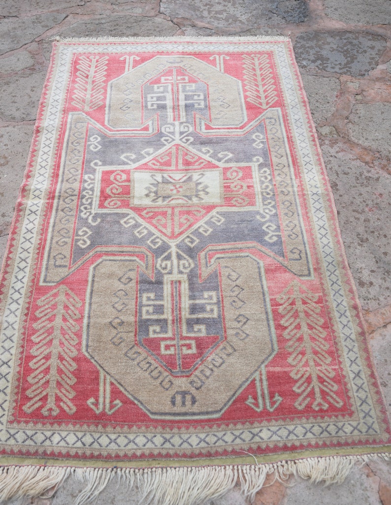 May include: A vintage Turkish rug with a geometric pattern in shades of red, beige, and gray. The rug has a fringe border and is woven with intricate details.