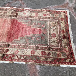 May include: A vintage Turkish rug with a red, beige, and brown color scheme. The rug has a traditional geometric pattern with a central medallion. The rug has a fringe border.