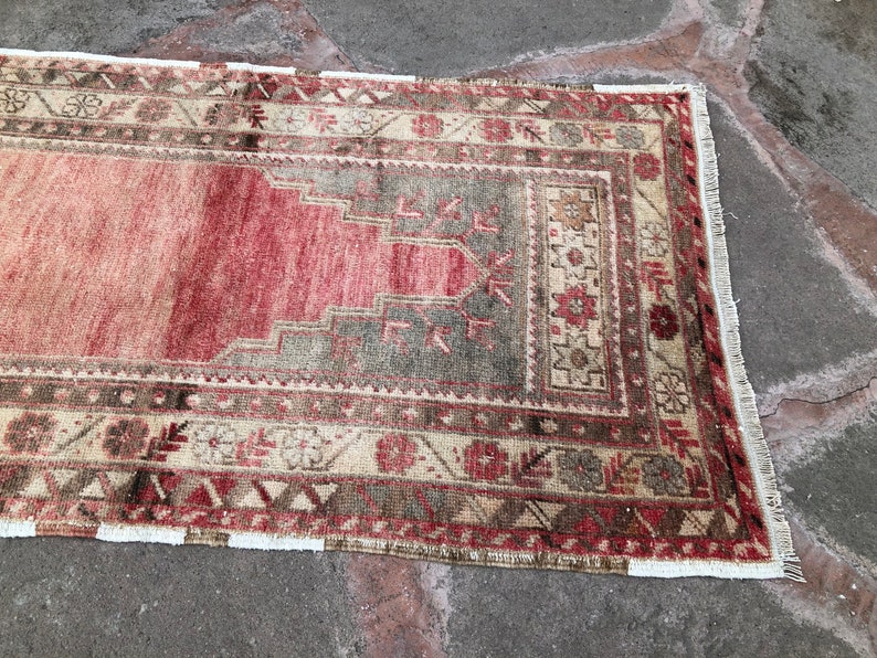 May include: A vintage Turkish rug with a red, beige, and brown color scheme. The rug has a traditional geometric pattern with a central medallion. The rug has a fringe border.