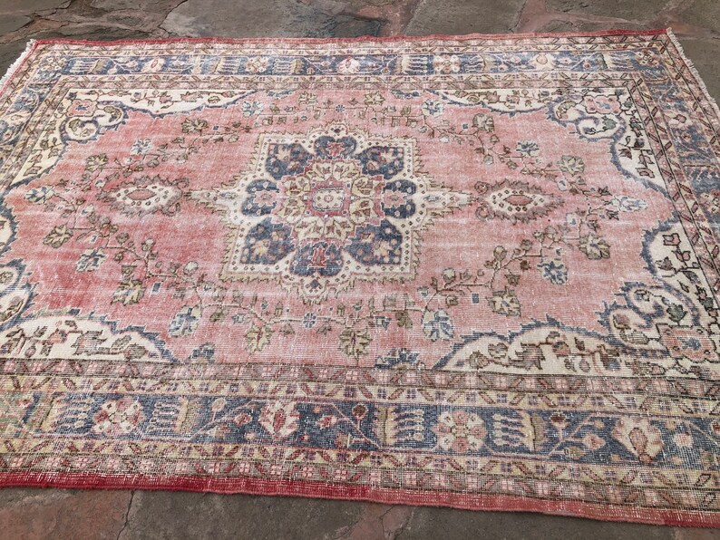 May include: A vintage rug with a faded pink background and intricate floral patterns in shades of blue, beige, and cream. The rug has a distressed look with a worn border.
