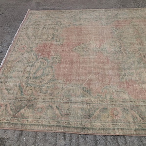 May include: A vintage rug with a faded pink and green floral pattern. The rug has a distressed look and is made of a soft, woven material.