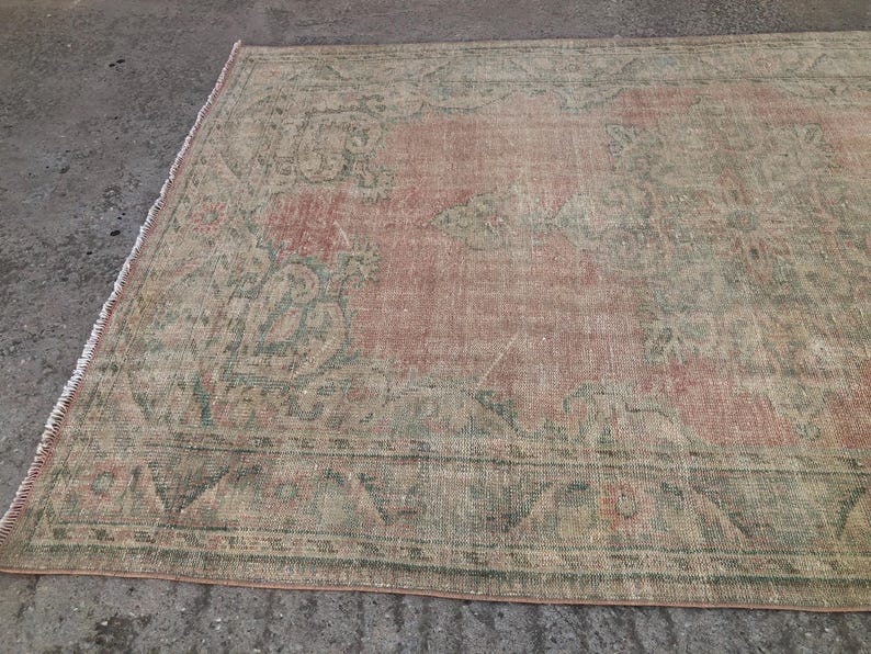 May include: A vintage rug with a faded pink and green floral pattern. The rug has a distressed look and is made of a soft, woven material.