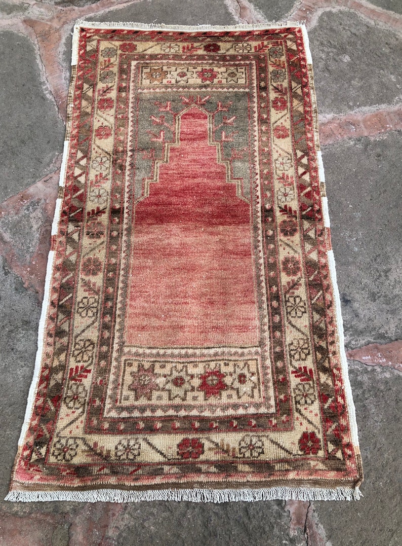 May include: A vintage Turkish prayer rug with a red, beige, and green geometric pattern. The rug has a fringe border and is in good condition.