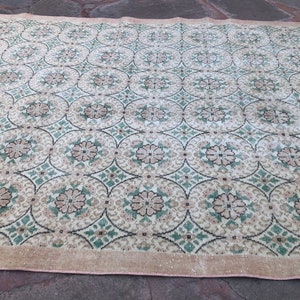 May include: A vintage rug with a repeating pattern of green, brown, and white floral motifs. The rug has a light beige background and a pink border.