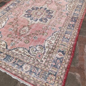 May include: A vintage pink and blue rug with a floral pattern and a central medallion. The rug has a fringed edge and is made of wool.