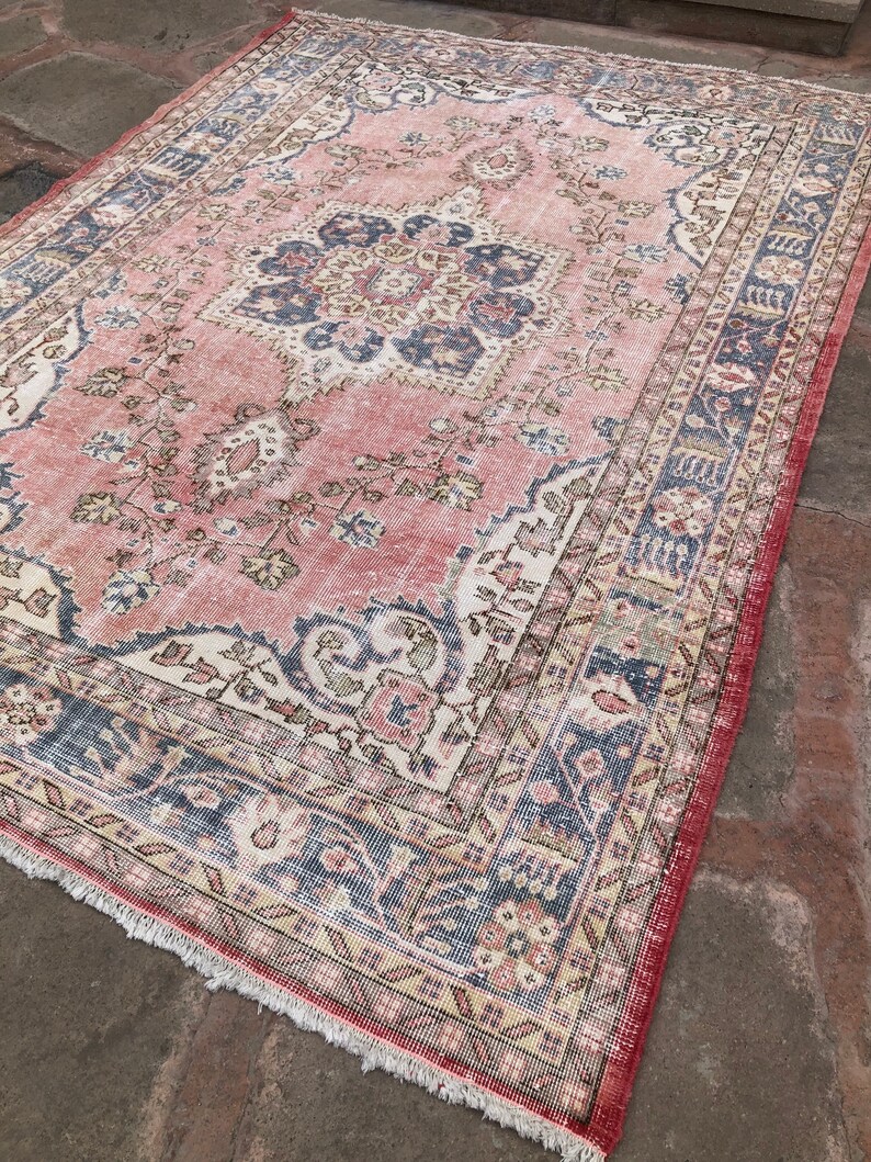 May include: A vintage pink and blue rug with a floral pattern and a central medallion. The rug has a fringed edge and is made of wool.