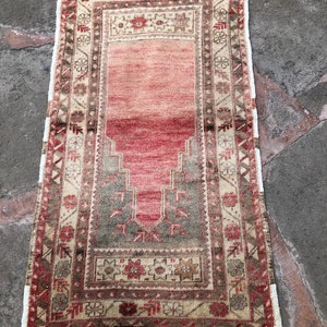 May include: A vintage Turkish prayer rug with a red, beige, and green geometric pattern. The rug has a fringe border and is in good condition.