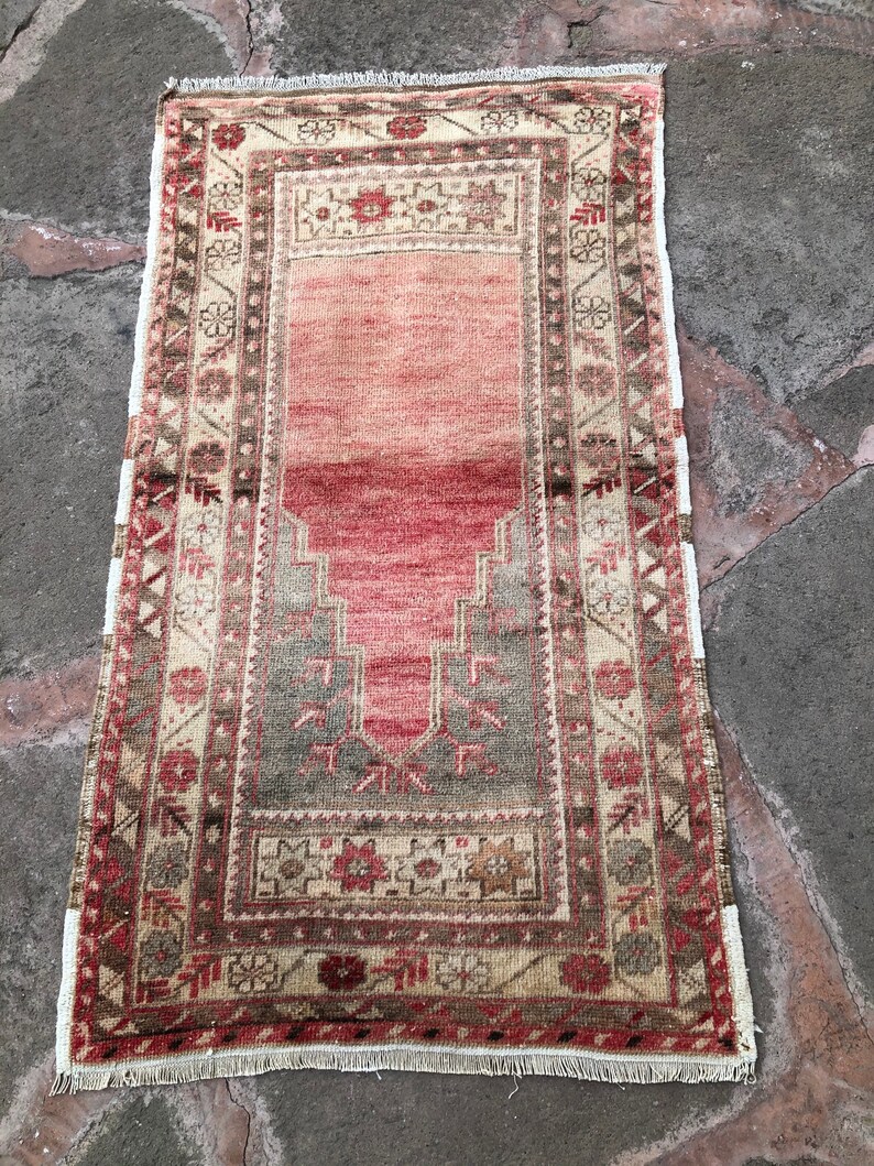 May include: A vintage Turkish prayer rug with a red, beige, and green geometric pattern. The rug has a fringe border and is in good condition.