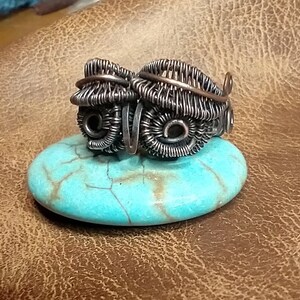 May include: Two silver wire wrapped rings with a copper wire accent. The rings are sitting on a turquoise stone.