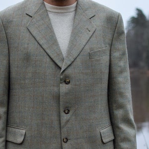 Puede incluir: Una chaqueta de tweed verde con cierre de tres botones. La chaqueta tiene un corte clásico y una tela ligeramente texturizada.