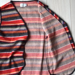 Könnte beinhalten: Eine gestreifte Weste mit schwarzem Besatz. Die Weste ist aus weichem, gewebtem Stoff gefertigt und hat eine lockere Passform. Die Weste ist vorne offen und hat einen V-Ausschnitt.