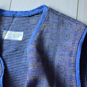 Könnte beinhalten: Eine blaue und braune gestreifte Weste mit blauem Besatz und einem Etikett mit der Aufschrift "Christina Kral".