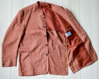 May include: A rust-colored linen blazer with a mandarin collar, four buttons, and a single patch pocket. The blazer is unlined and has a brown zipper closure. The inside of the blazer is a rust-colored satin. The label inside the blazer reads "MFC".