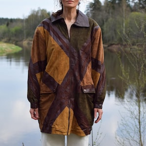Peut inclure: Veste vintage en daim dans les tons marron, beige et vert olive. La veste présente un motif géométrique et un col marron foncé. Elle possède deux poches avant et une fermeture éclair. La veste arrive aux genoux.