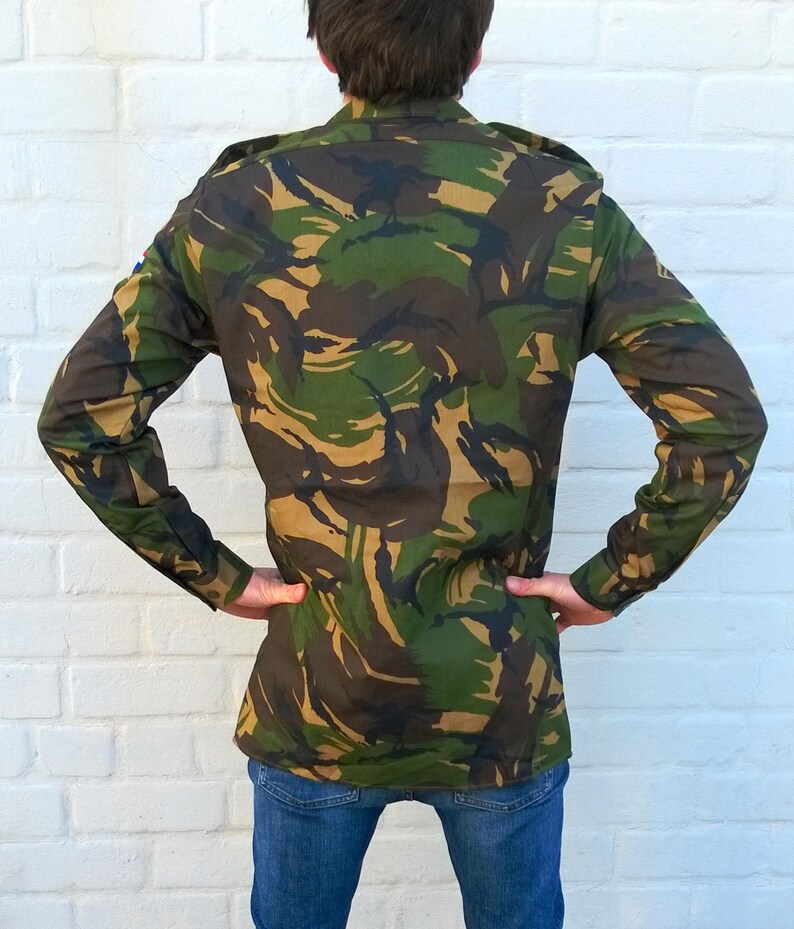 May include: A long-sleeved camouflage shirt with a button-up collar. The shirt has a dark green, brown, and tan camouflage pattern.