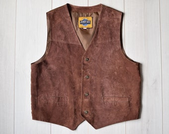 May include: A brown suede waistcoat with a V-neck and four buttons down the front. The waistcoat has two front pockets and a label that reads "JOHN F. GEE". The garment is displayed on a white wooden surface.