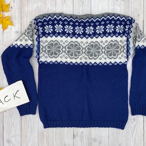 Puede incluir: Un suéter de punto azul con un diseño estampado blanco y gris. El suéter tiene mangas largas y cuello redondo.