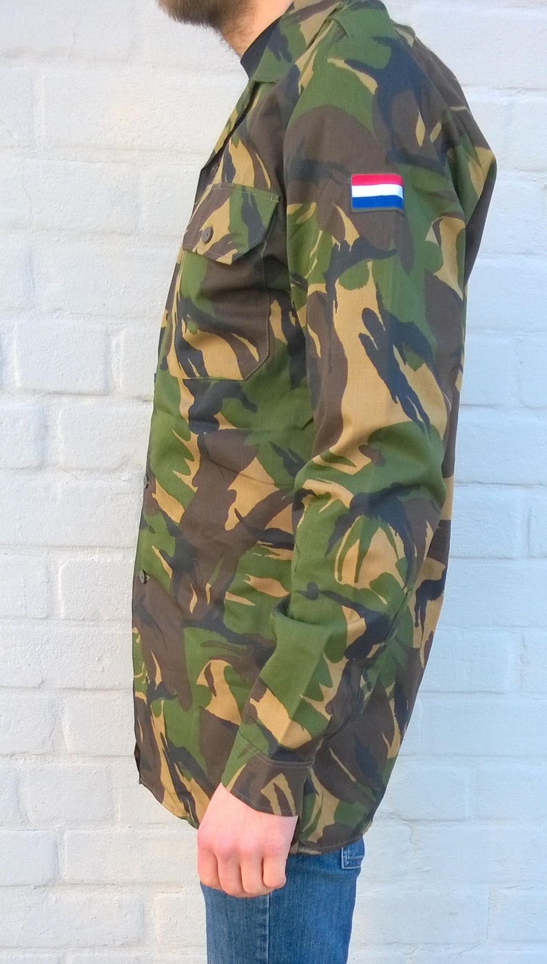May include: A camouflage long-sleeved shirt with a Dutch flag patch on the sleeve.