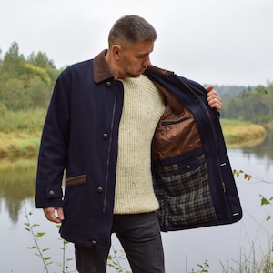 Può includere: Un cappotto blu navy con colletto marrone e finiture marroni sulle tasche. Il cappotto presenta una chiusura frontale con bottoni e una fodera interna parzialmente marrone tinta unita e parzialmente a quadri verdi, blu e marroni.