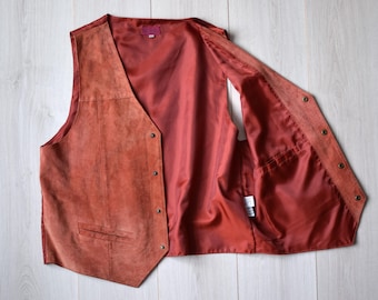 May include: A rust-colored suede vest with a button closure and a pocket on the front. The vest is unlined and has a smooth, silky lining.