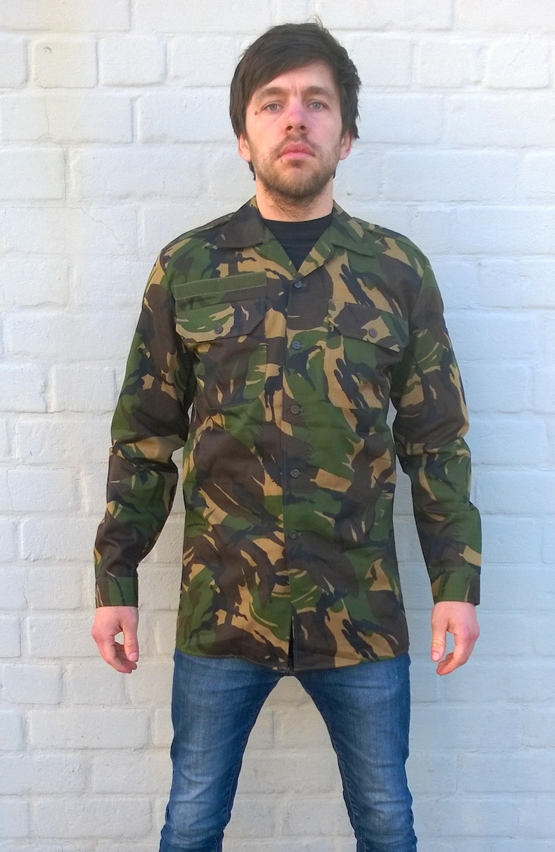 May include: A long-sleeved camouflage shirt with a button-down collar. The shirt has a green, brown, and black camouflage pattern.