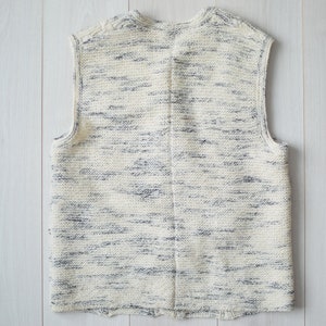 May include: A sleeveless knitted vest in a cream color with a subtle blue and white marbled pattern.