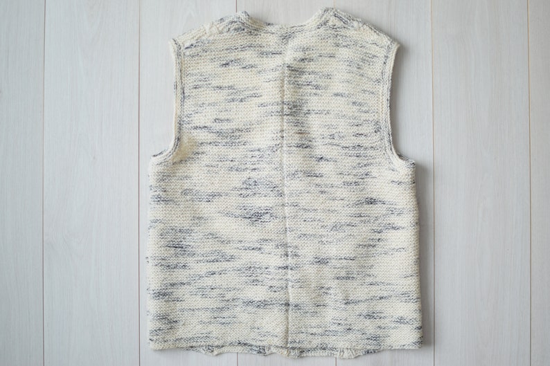 May include: A sleeveless knitted vest in a cream color with a subtle blue and white marbled pattern.