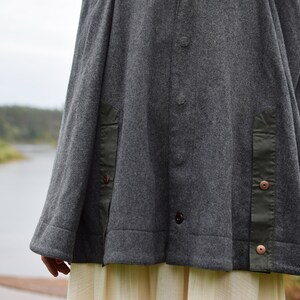 May include: A gray wool jacket with a green fabric detail on the sides. The jacket has a button closure and a relaxed fit.