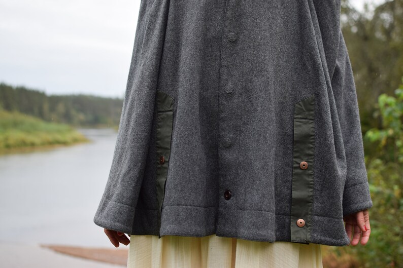 May include: A gray wool jacket with a green fabric detail on the sides. The jacket has a button closure and a relaxed fit.