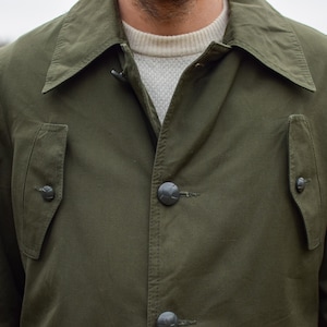 May include: A dark green jacket with a button fastening and two flap pockets. The jacket has a collar that can be folded up.