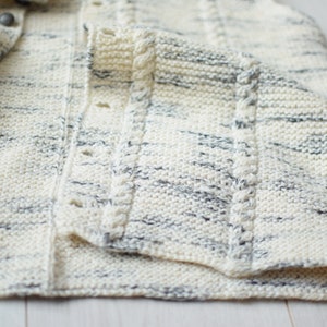May include: A white and gray knitted cardigan with a button closure and a cable knit detail on the front.