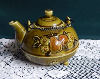 May include: A brown ceramic teapot with a floral and fruit design. The teapot has a spring-loaded lid and a wire handle.