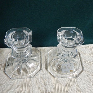 May include: Two clear glass candle holders with a square base and a starburst design. The candle holders are made by Mikasa.