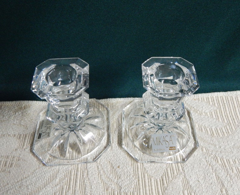May include: Two clear glass candle holders with a square base and a starburst design. The candle holders are made by Mikasa.