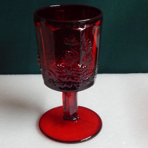 May include: A red glass stemmed goblet with a floral design. The goblet has a wide base and a tall, slender stem.