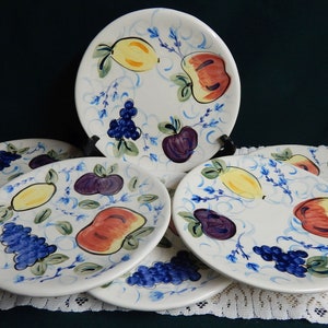 May include: Set of five white ceramic plates with hand-painted fruit designs. The plates feature apples, pears, grapes, and plums in shades of red, yellow, blue, and purple.