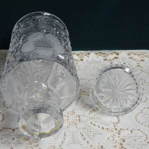 May include: A clear glass decanter with a textured design and a matching stopper. The decanter has a wide base and a narrow neck.