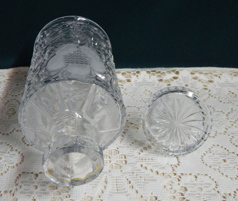 May include: A clear glass decanter with a textured design and a matching stopper. The decanter has a wide base and a narrow neck.