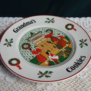 May include: White ceramic plate with a red rim. The plate features a Christmas scene with a family baking cookies in the kitchen. The text "Grandma's Cookies" is written on the plate.